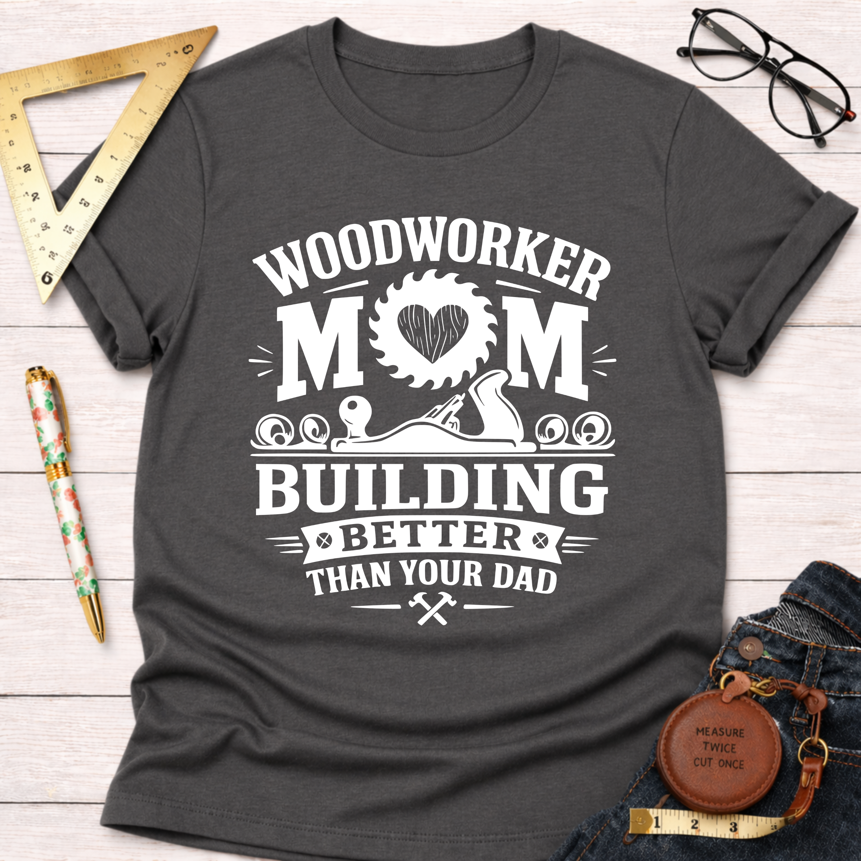 Women's funny woodworking graphic tee shirt for female woodworkers, makers, and DIY builders — Sawdust & Ponytails. Dark gray crewneck t-shirt with "Woodworker Mom Building Better Than Your Dad" graphic.