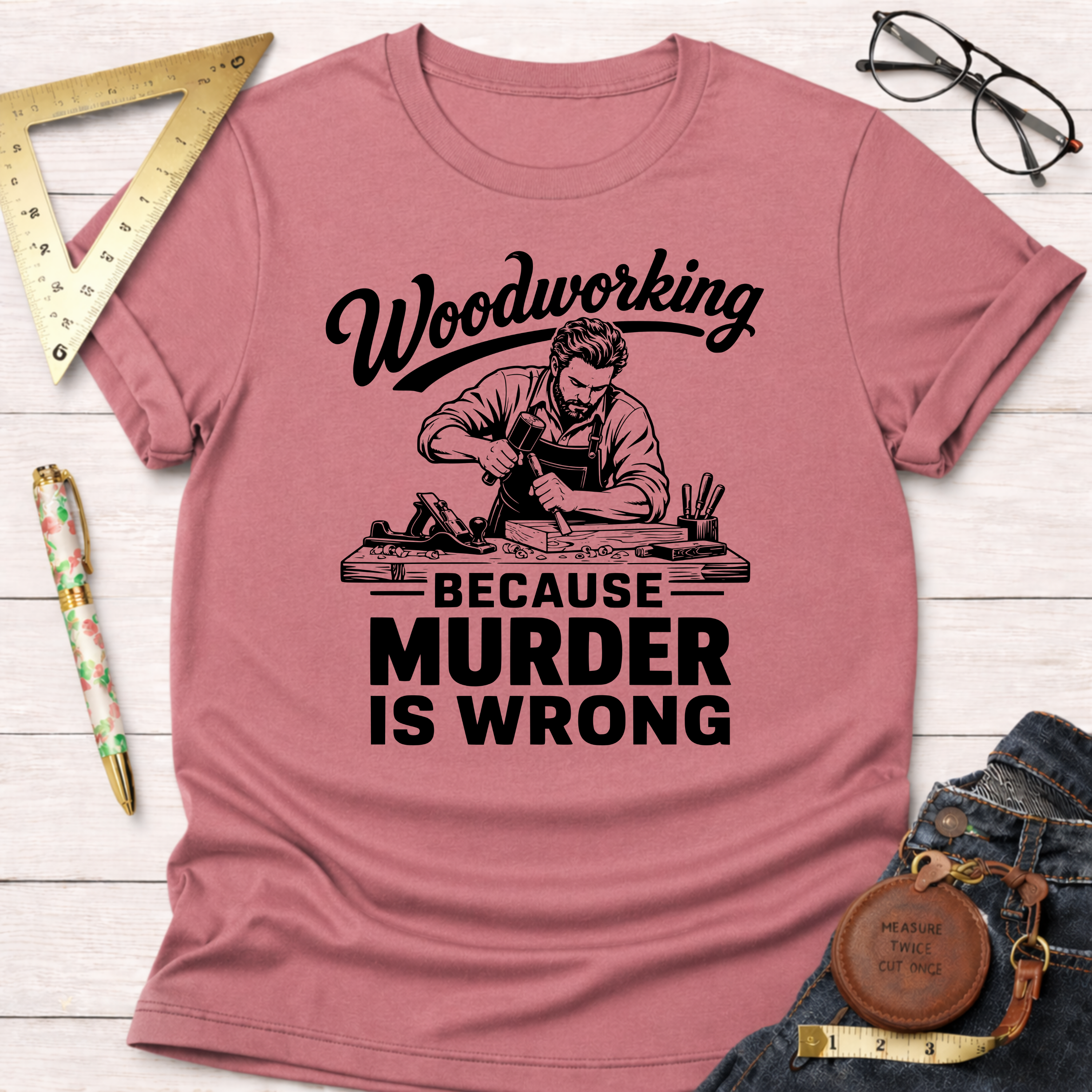 Pink short-sleeve t-shirt with "Woodworking Because Murder Is Wrong" graphic featuring a carpenter.