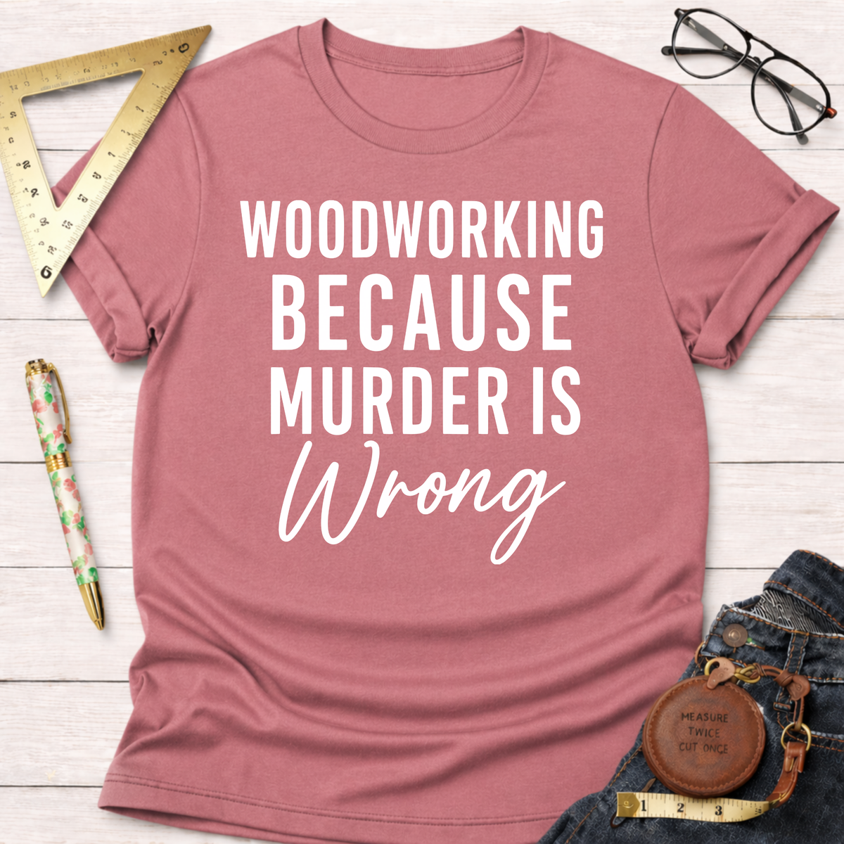 Heather mauve t-shirt with "WOODWORKING BECAUSE MURDER IS WRONG" in white text, styled with jeans and tools.