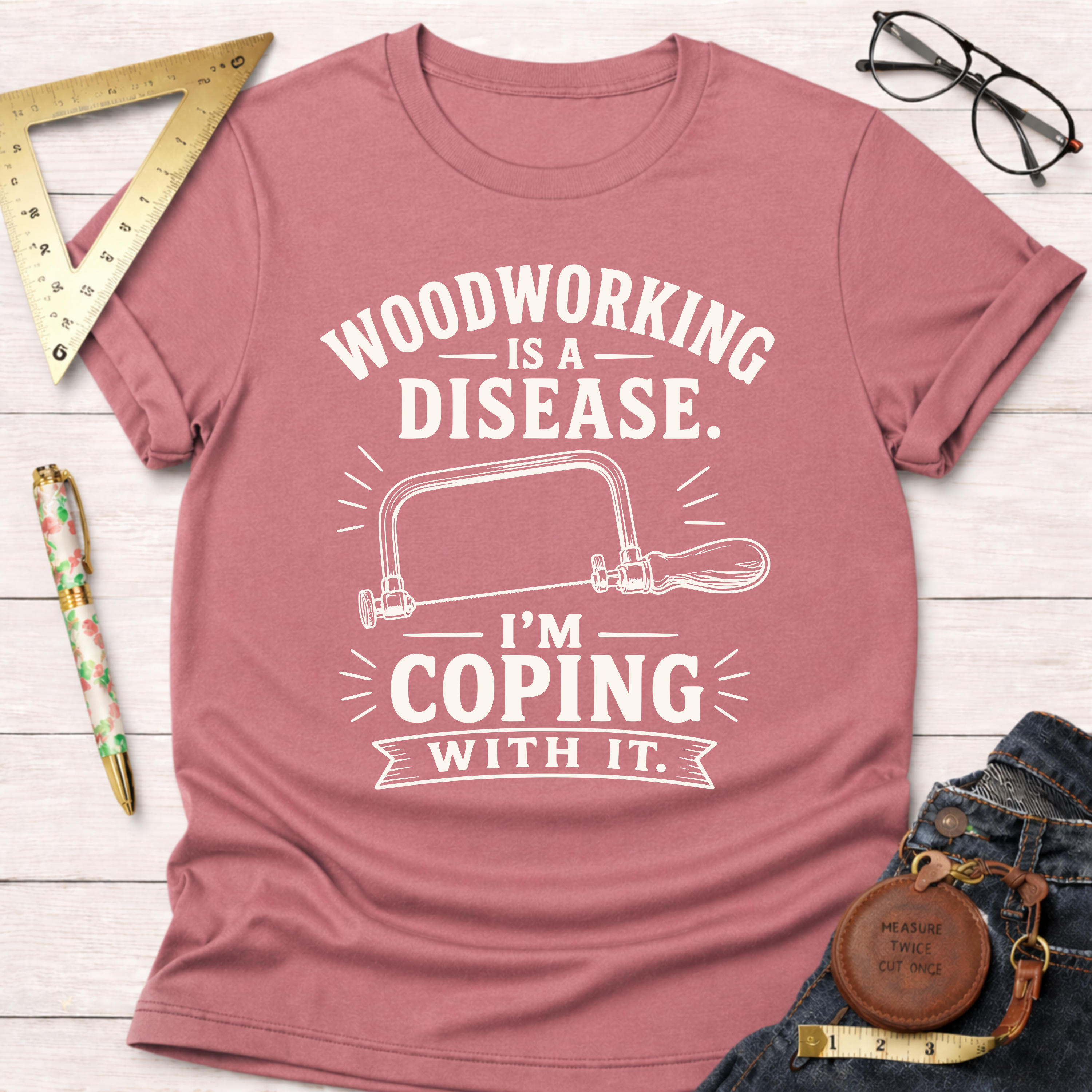 Women's funny woodworking graphic tee shirt for female woodworkers, makers, and DIY builders — Sawdust & Ponytails. Heather mauve t-shirt with "Woodworking Is A Disease. I'm Coping With It." text and a hand saw graphic.