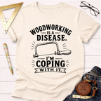 Women's funny woodworking graphic tee shirt for female woodworkers, makers, and DIY builders — Sawdust & Ponytails. Cream cotton tee with "Woodworking Is A Disease. I'm Coping With It." text and a coping saw graphic.