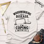 Women's funny woodworking graphic tee shirt for female woodworkers, makers, and DIY builders — Sawdust & Ponytails. Cream t-shirt with "Woodworking Is A Disease. I'm Coping With It." text and a hand saw graphic.