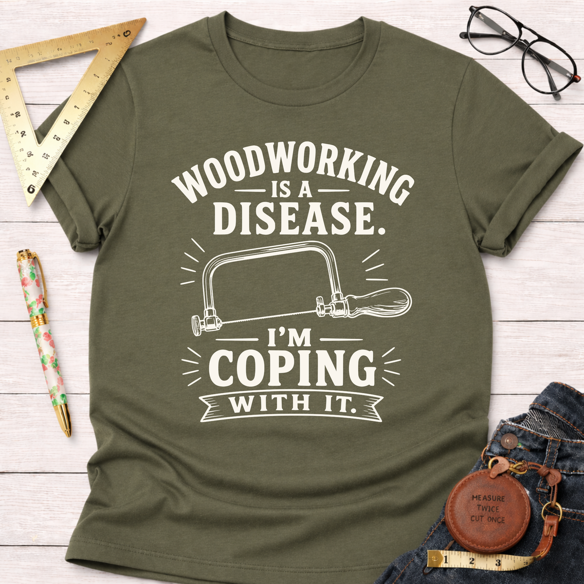 Women's funny woodworking graphic tee shirt for female woodworkers, makers, and DIY builders — Sawdust & Ponytails. Olive green cotton tee with "Woodworking Is A Disease. I'm Coping With It." text and hand saw graphic.