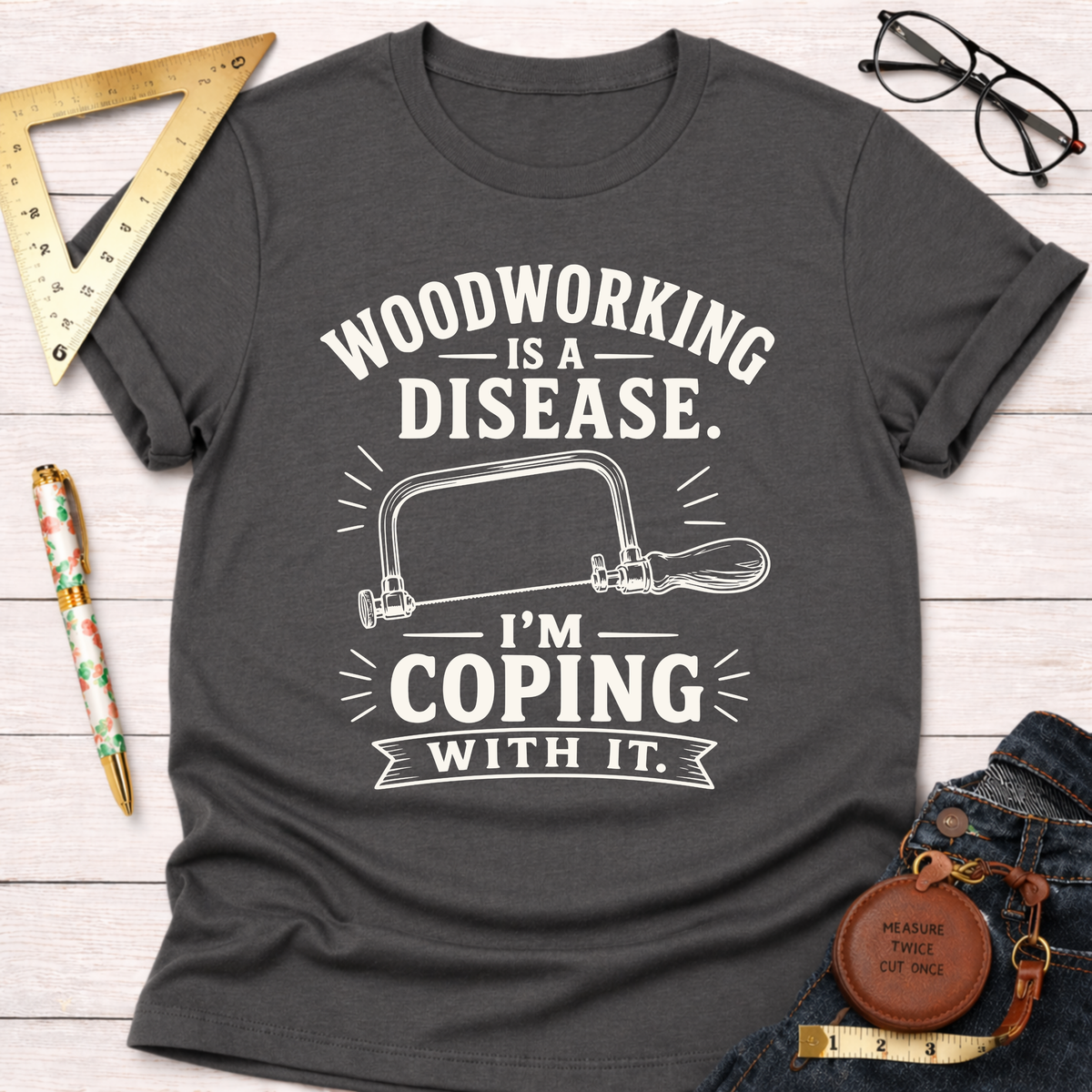 Women's funny woodworking graphic tee shirt for female woodworkers, makers, and DIY builders — Sawdust & Ponytails. Dark gray cotton tee with "Woodworking Is A Disease. I'm Coping With It." text and a hand saw graphic.