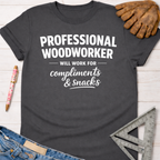 Women's funny woodworking graphic tee shirt for female woodworkers, makers, and DIY builders — Sawdust & Ponytails. Dark gray cotton tee with "Professional Woodworker Will Work For Compliments & Snacks" in white text.