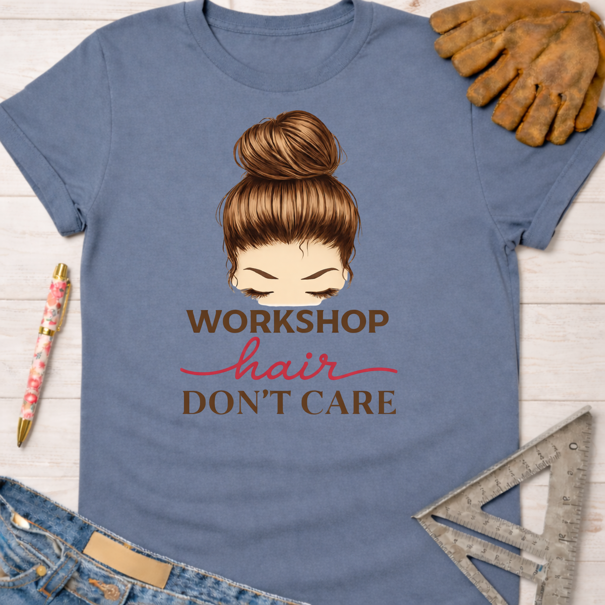 Women's funny woodworking graphic tee shirt for female woodworkers, makers, and DIY builders — Sawdust & Ponytails. Blue cotton tee with a messy bun graphic and "Workshop Hair Don't Care" text.