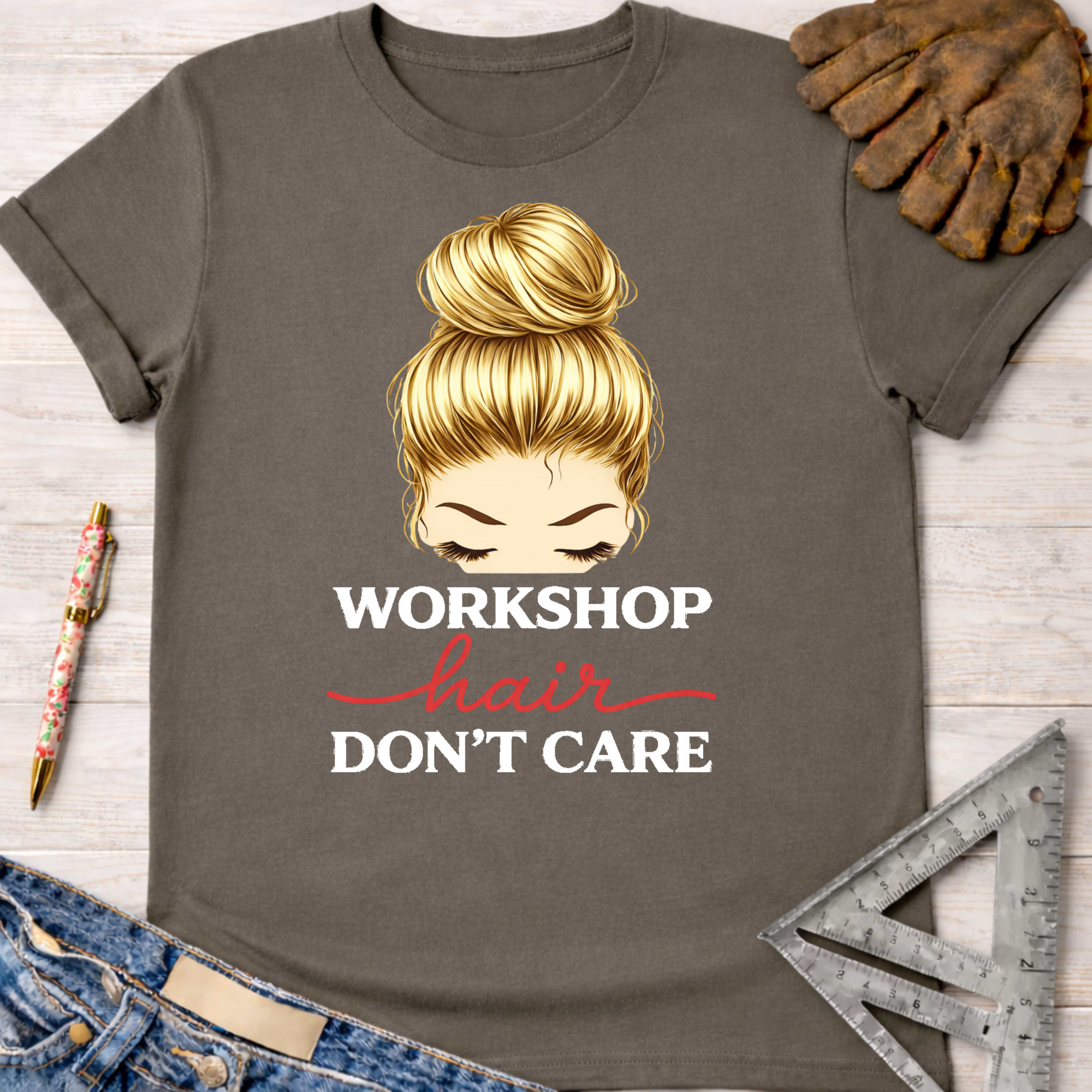 Women's funny woodworking graphic tee shirt for female woodworkers, makers, and DIY builders — Sawdust & Ponytails. Dark gray cotton t-shirt with blonde messy bun graphic and "Workshop Hair Don't Care" text.