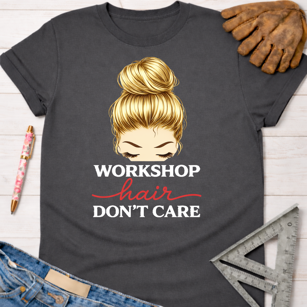 Women's funny woodworking graphic tee shirt for female woodworkers, makers, and DIY builders — Sawdust & Ponytails. Dark gray t-shirt with blonde messy bun graphic and "Workshop Hair Don't Care" text.
