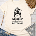 Women's funny woodworking graphic tee shirt for female woodworkers, makers, and DIY builders — Sawdust & Ponytails. Cream cotton tee with "Workshop Hair Don't Care" graphic of a messy bun and sunglasses.