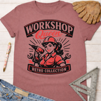 Women's funny woodworking graphic tee shirt for female woodworkers, makers, and DIY builders — Sawdust & Ponytails. Retro pink tee with "Workshop Queen" text and a woman holding a drill.