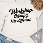 Women's funny woodworking graphic tee shirt for female woodworkers, makers, and DIY builders — Sawdust & Ponytails. Cream t-shirt with "Workshop therapy hits different" in black script, next to jeans, a pen, work glove, and ruler.