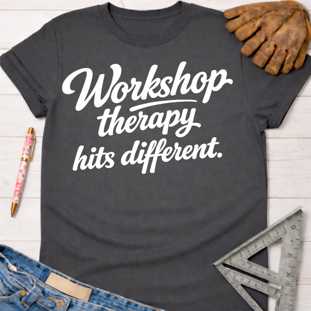 Women's funny woodworking graphic tee shirt for female woodworkers, makers, and DIY builders — Sawdust & Ponytails. Dark gray t-shirt with "Workshop therapy hits different" in white script.