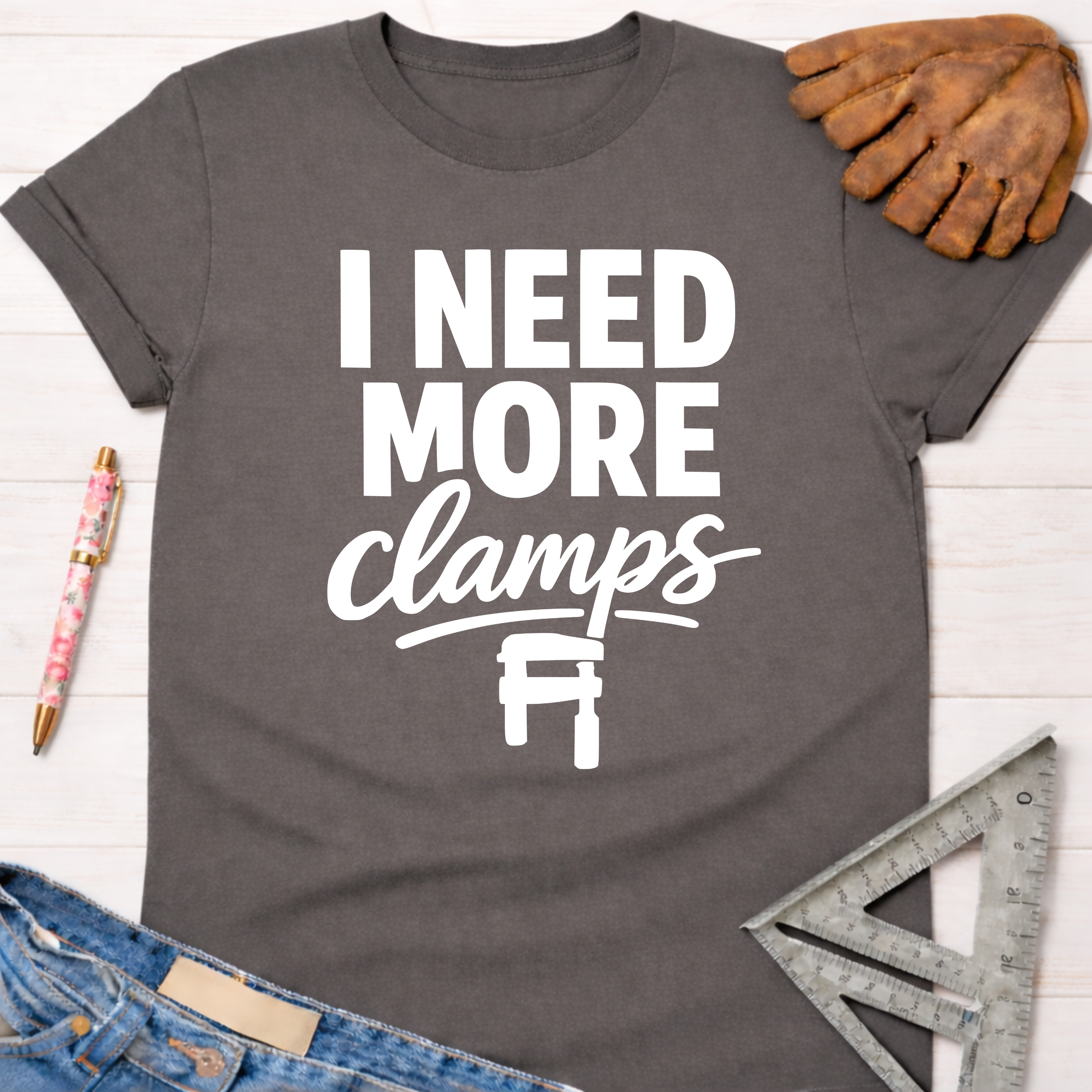 Women's funny woodworking graphic tee shirt for female woodworkers, makers, and DIY builders — Sawdust & Ponytails. Dark gray cotton t-shirt with "I NEED MORE clamps" text and clamp graphic.