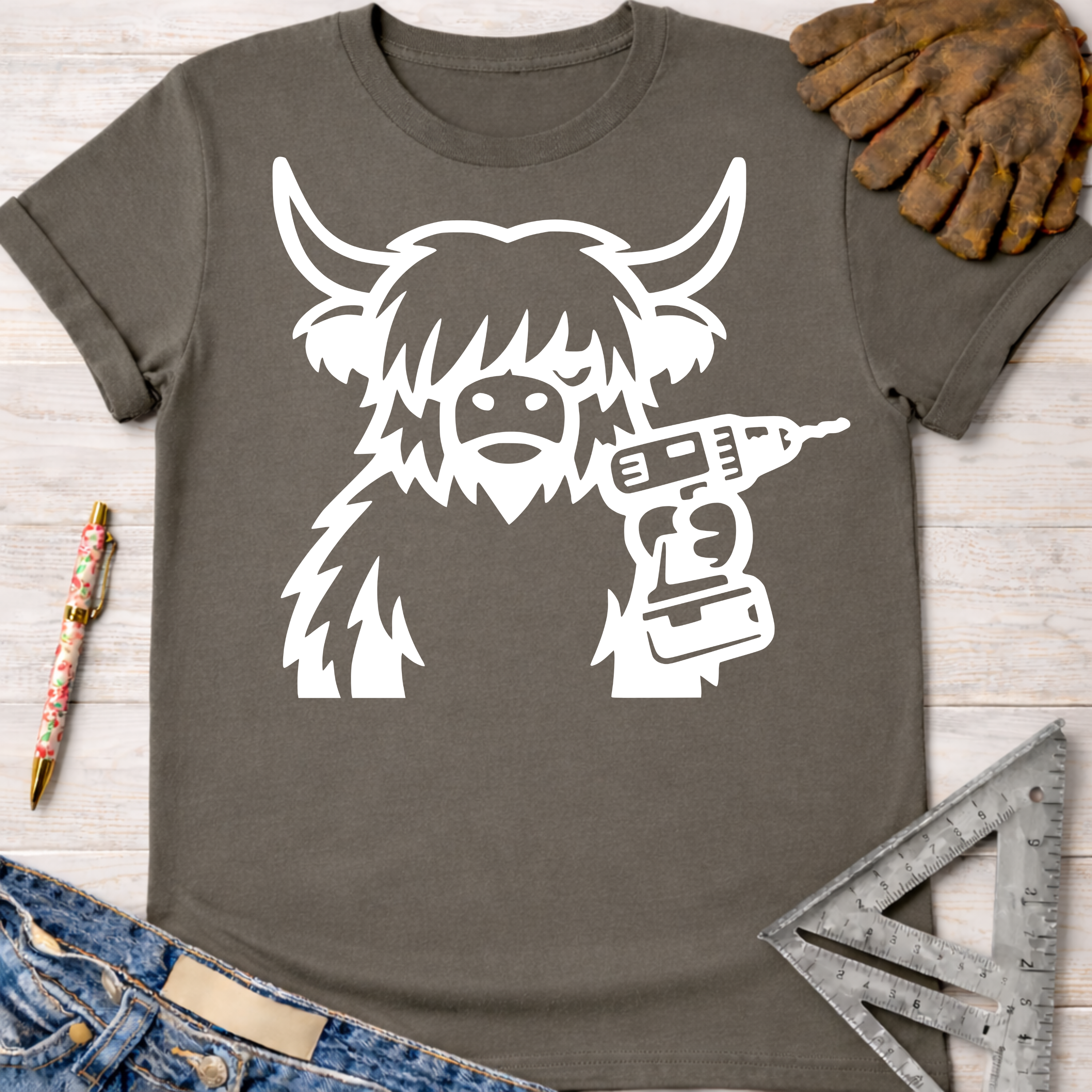 Women's funny woodworking graphic tee shirt for female woodworkers, makers, and DIY builders — Sawdust & Ponytails. Dark gray t-shirt with a white graphic of a shaggy cow holding a drill.