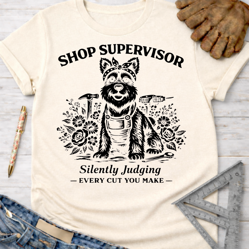 Women's funny woodworking graphic tee shirt for female woodworkers, makers, and DIY builders — Sawdust & Ponytails. Cream t-shirt with a black graphic of a dog in a bandana and overalls, surrounded by tools and flowers, with "Shop Supervisor Silently Judging Every Cut You Make" text.